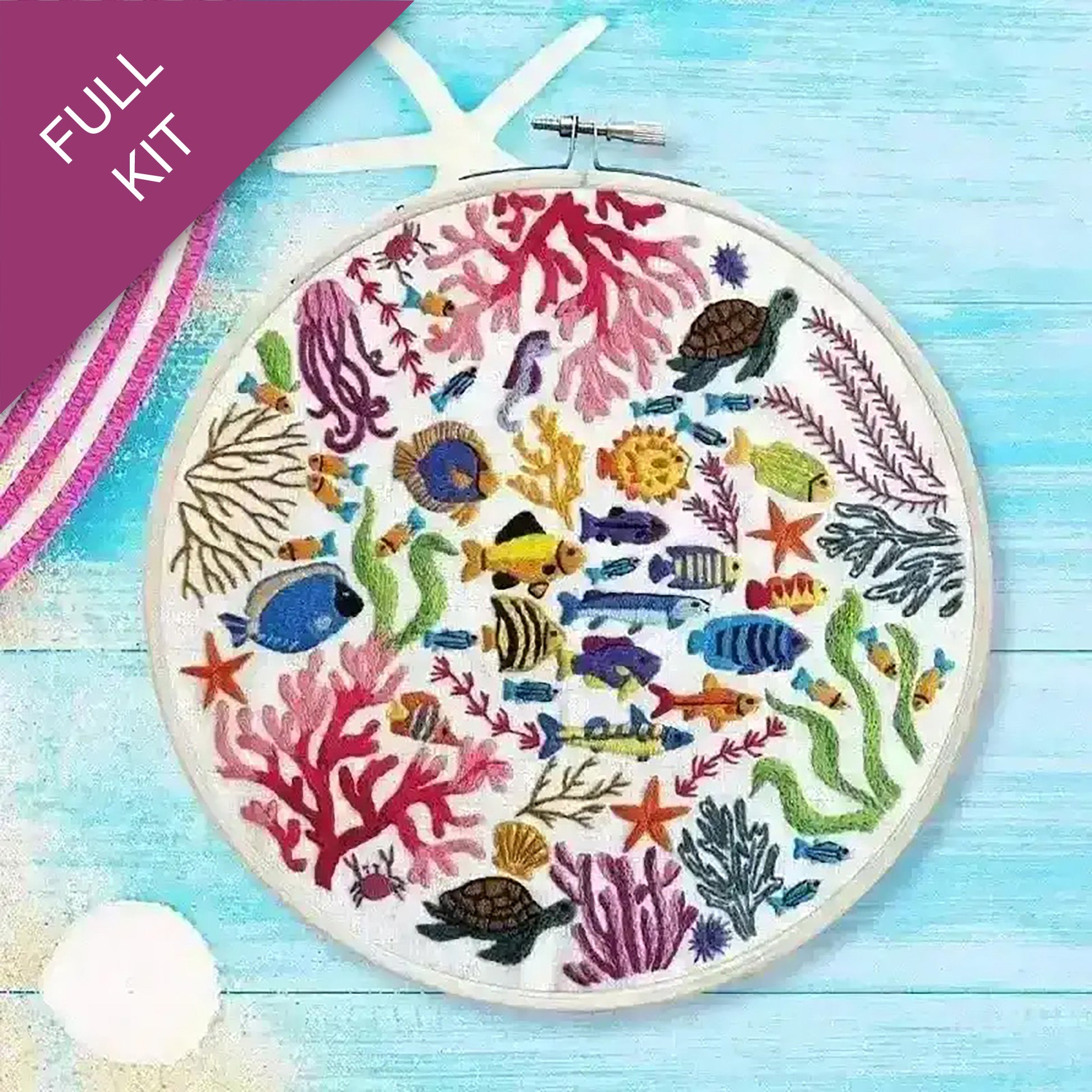 Embroidery hoop with colorful underwater scene including fish, corals, and sea turtles on a blue wooden surface.