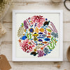 Framed artwork of colorful sea creatures and coral on a wooden surface with crafting supplies.