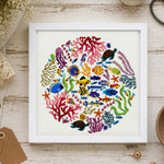 Framed artwork of colorful sea creatures and coral on a wooden surface with crafting supplies.