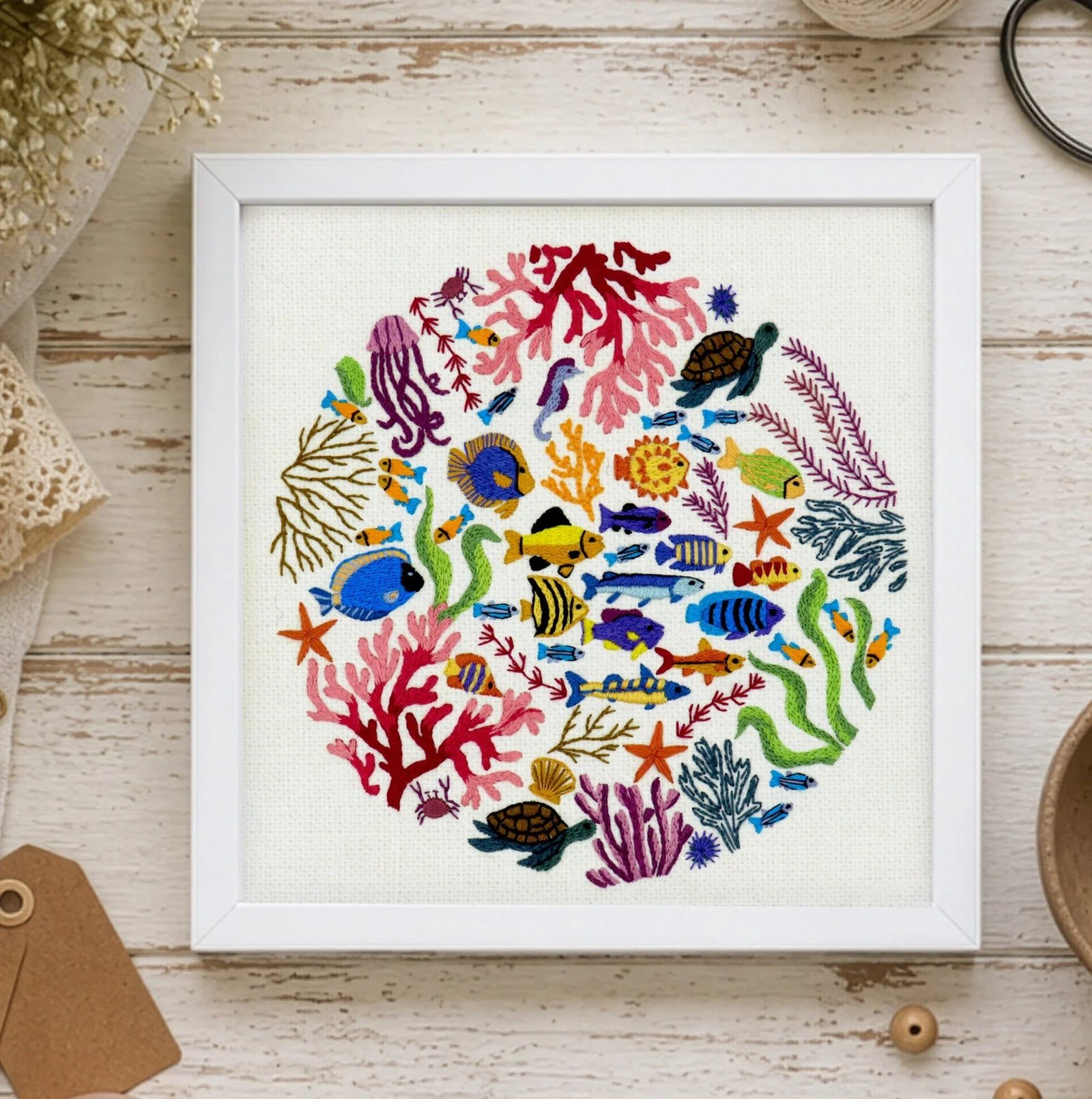 Framed artwork of colorful sea creatures and coral on a wooden surface with crafting supplies.