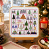 Cross-stitch pattern with Christmas trees on a stand, surrounded by festive decor including a tree, lantern, and candles.
