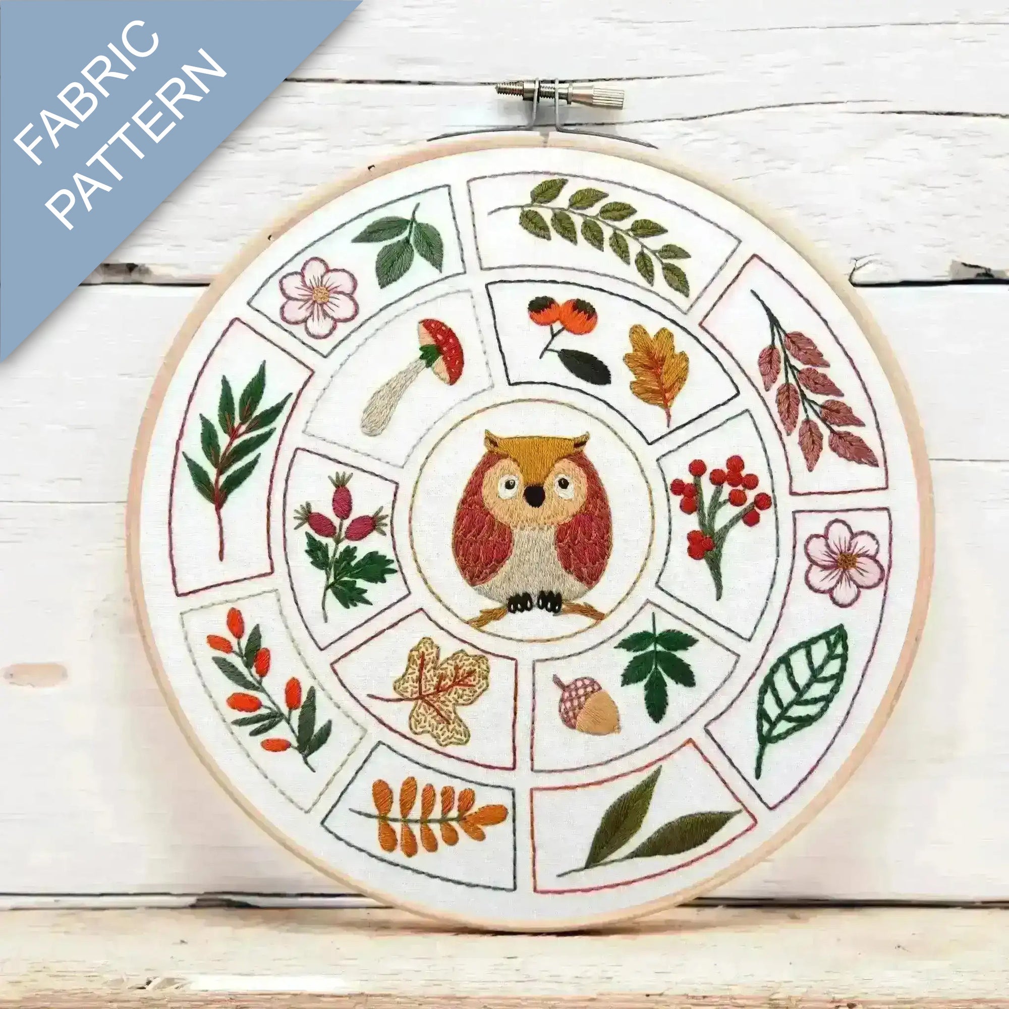 Embroidery hoop with a fabric pattern featuring an owl and nature elements on a wooden surface.