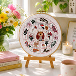 Decorative embroidery hoop with floral and owl design on a table with books, flowers, and a cup.