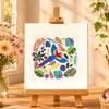 Colorful artwork on a small easel with a cup, notebook, and flowers in the background.