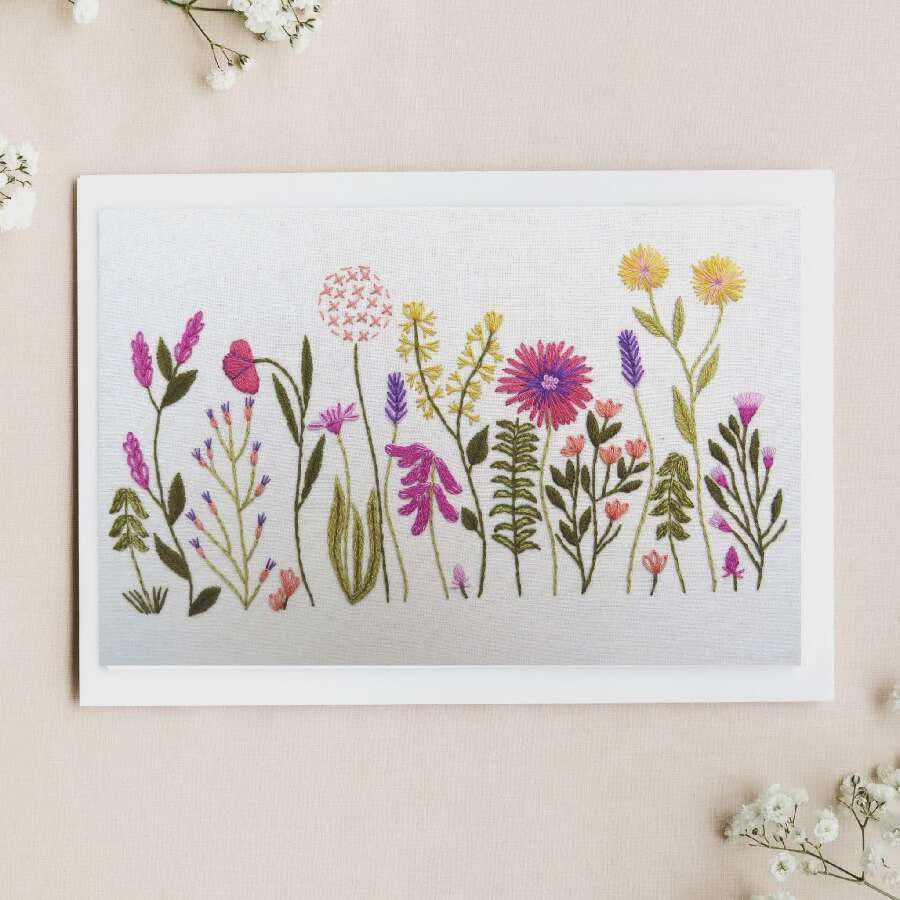 Framed artwork of colorful flowers on a white surface with a vase of real flowers.