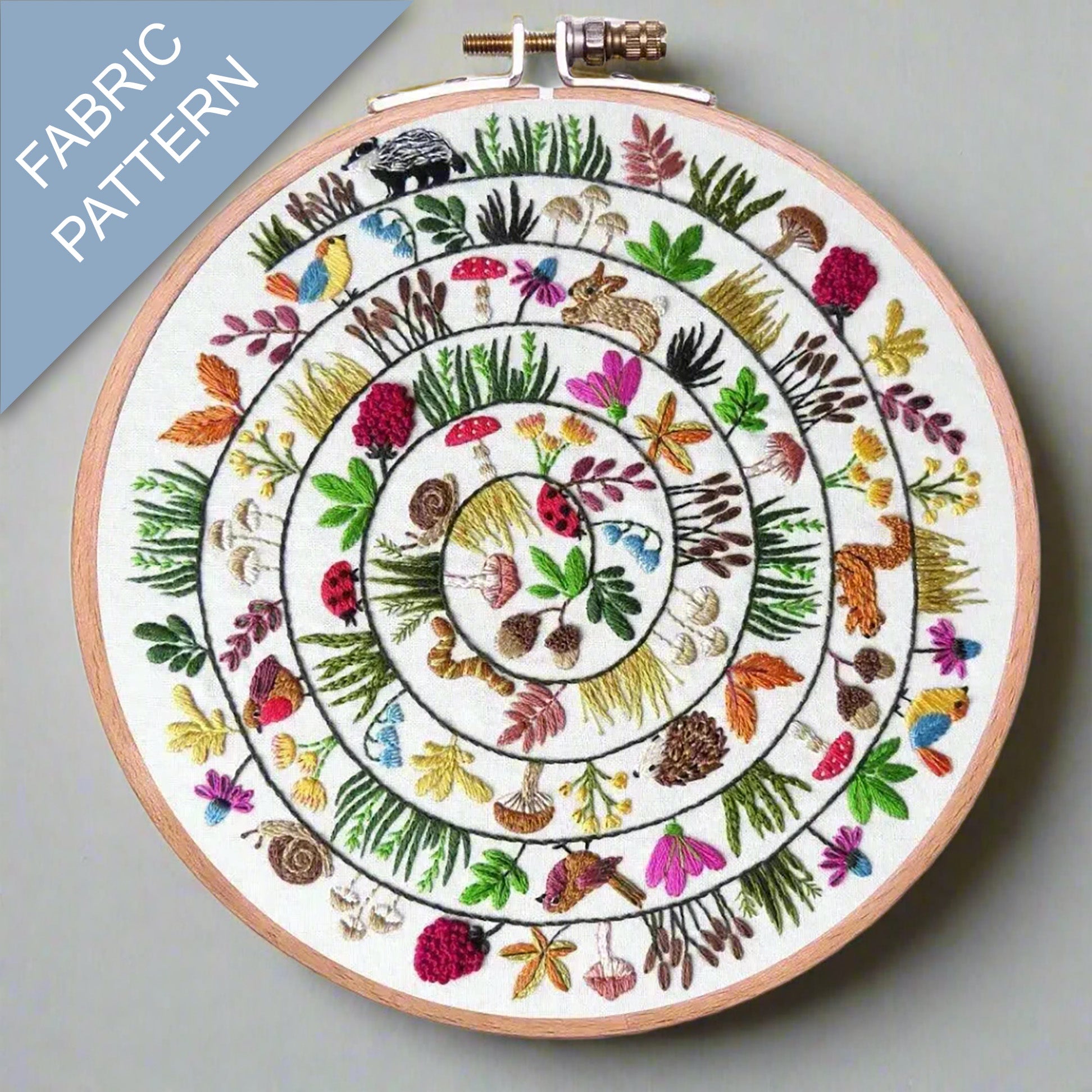 Embroidery hoop with a colorful fabric pattern featuring animals and plants on a light gray background.