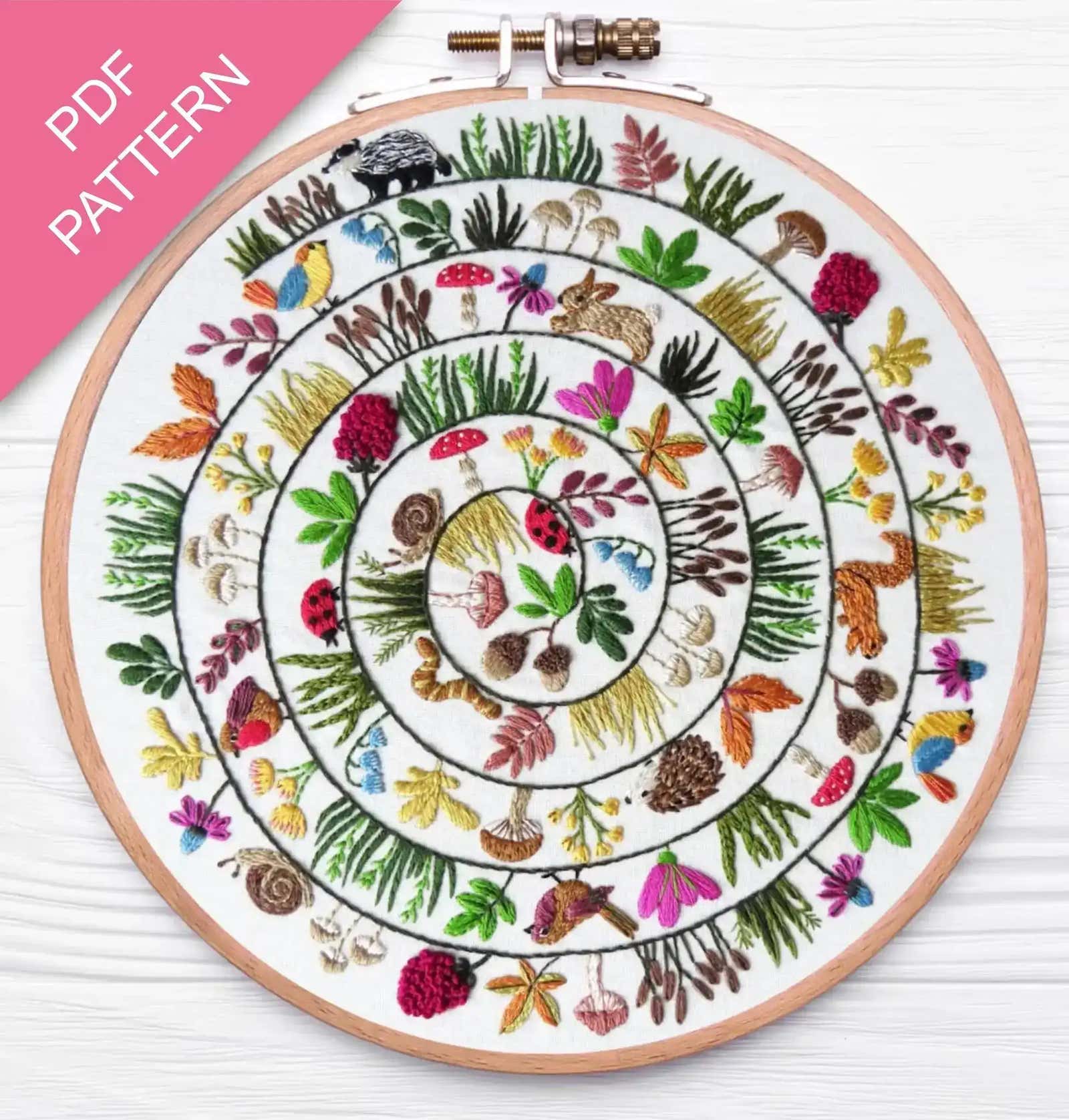 Embroidery hoop with a colorful circular pattern of animals and plants on a white background.