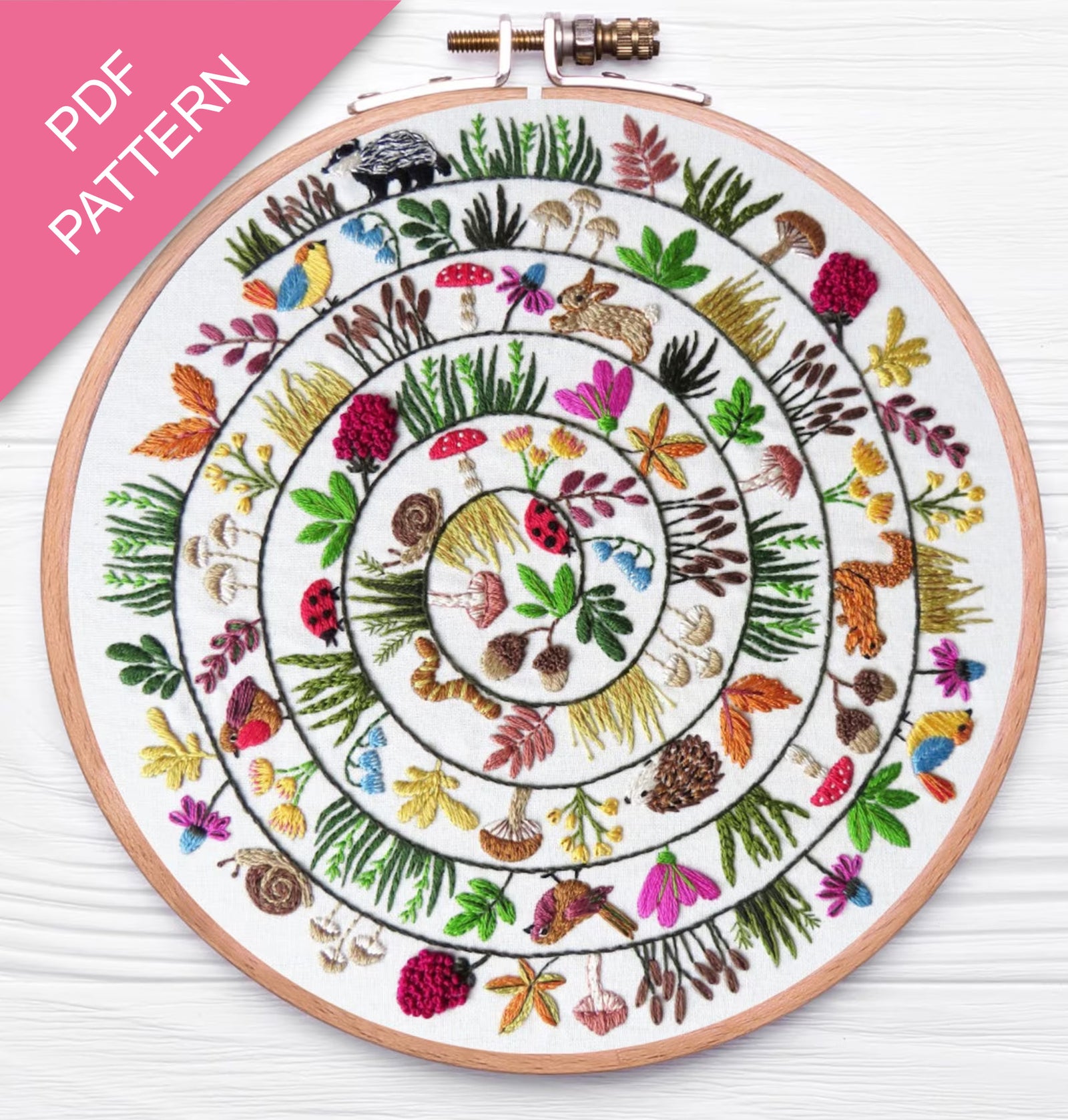 Embroidery hoop with a colorful circular pattern of animals and plants on a white background.