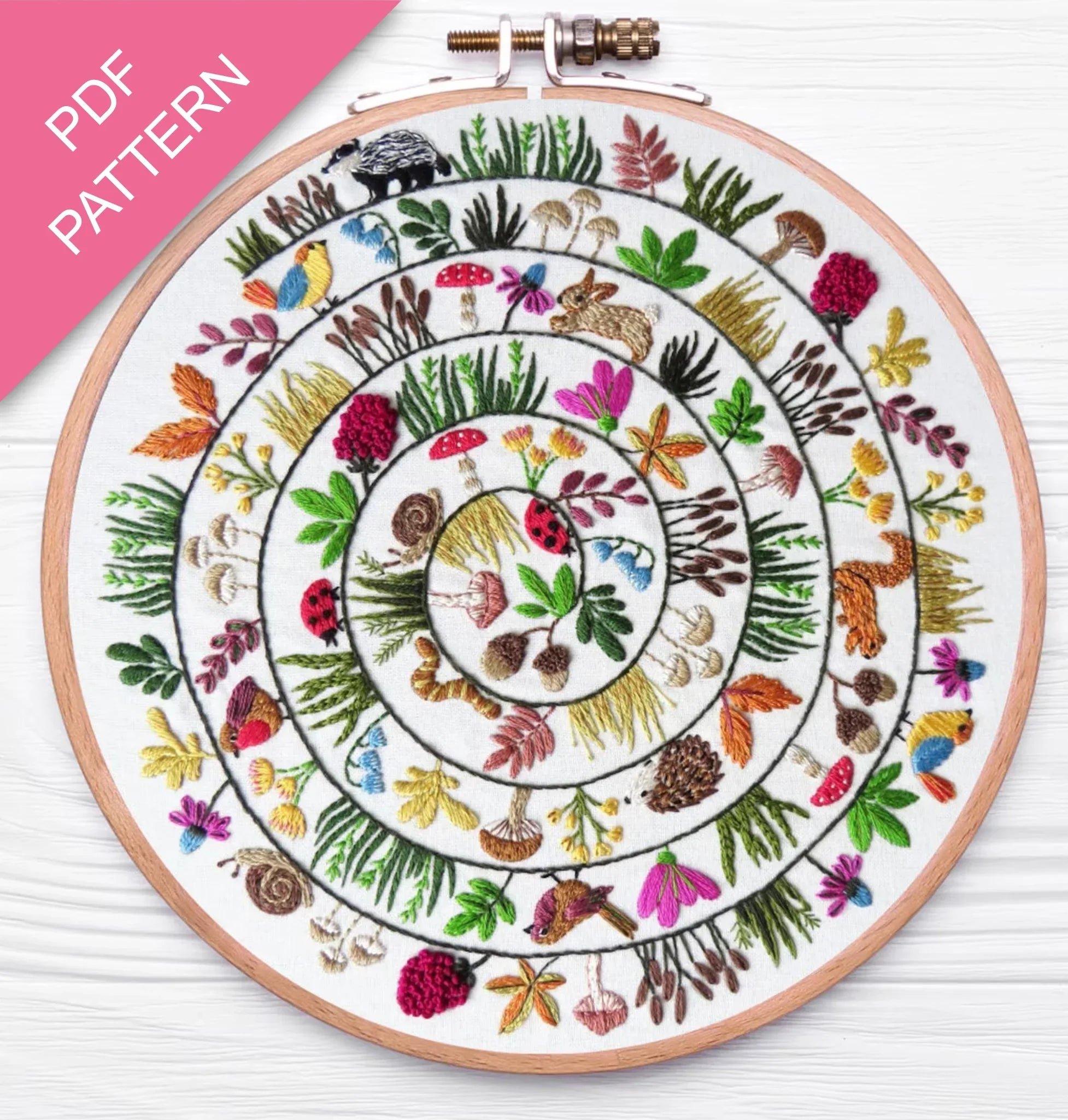 Embroidery hoop with a colorful circular pattern of animals and plants on a white background.
