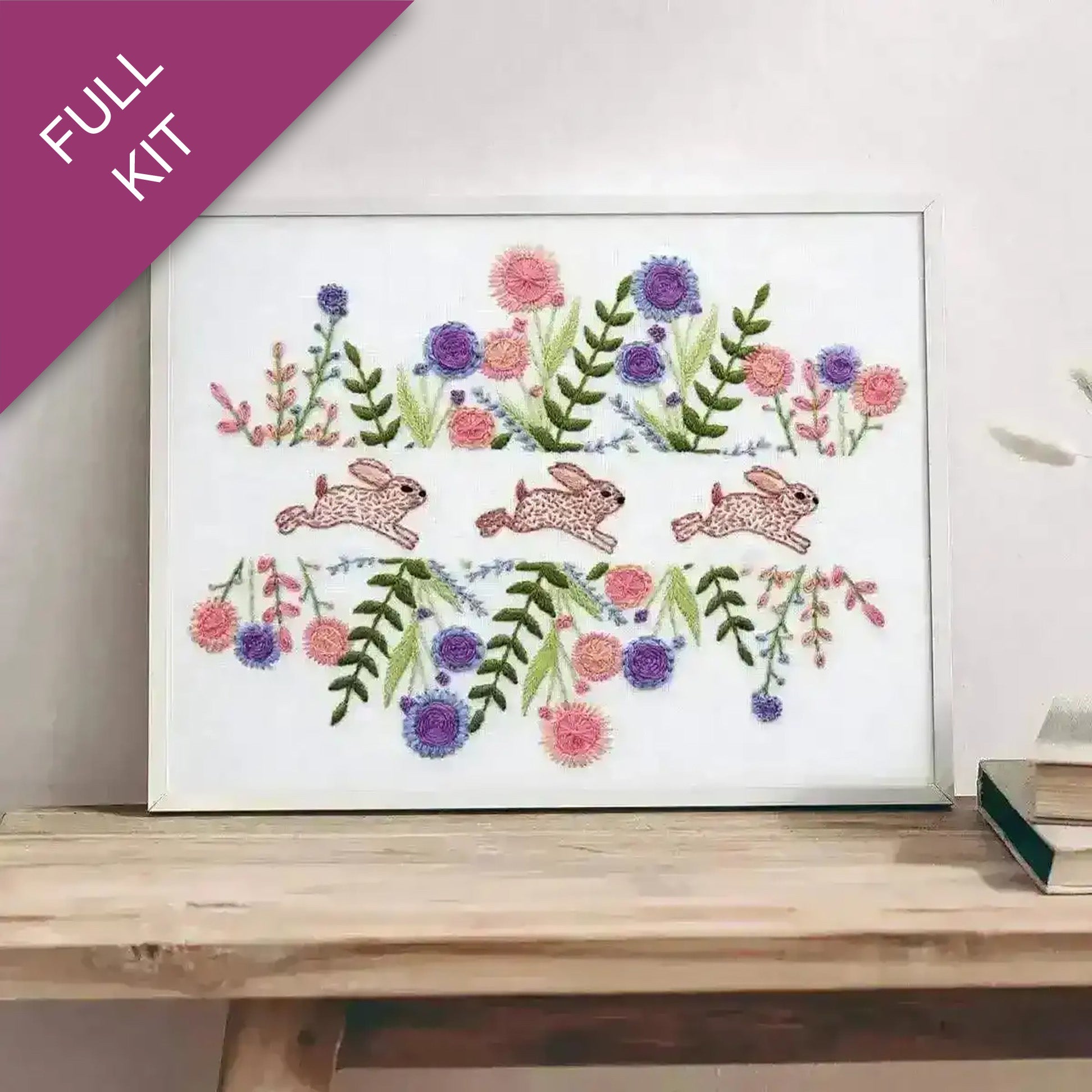 Embroidery design with bunnies and flowers on a white background, framed and displayed on a wooden surface.