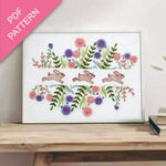 Embroidery design with bunnies and flowers on a white background, framed and displayed on a wooden surface.