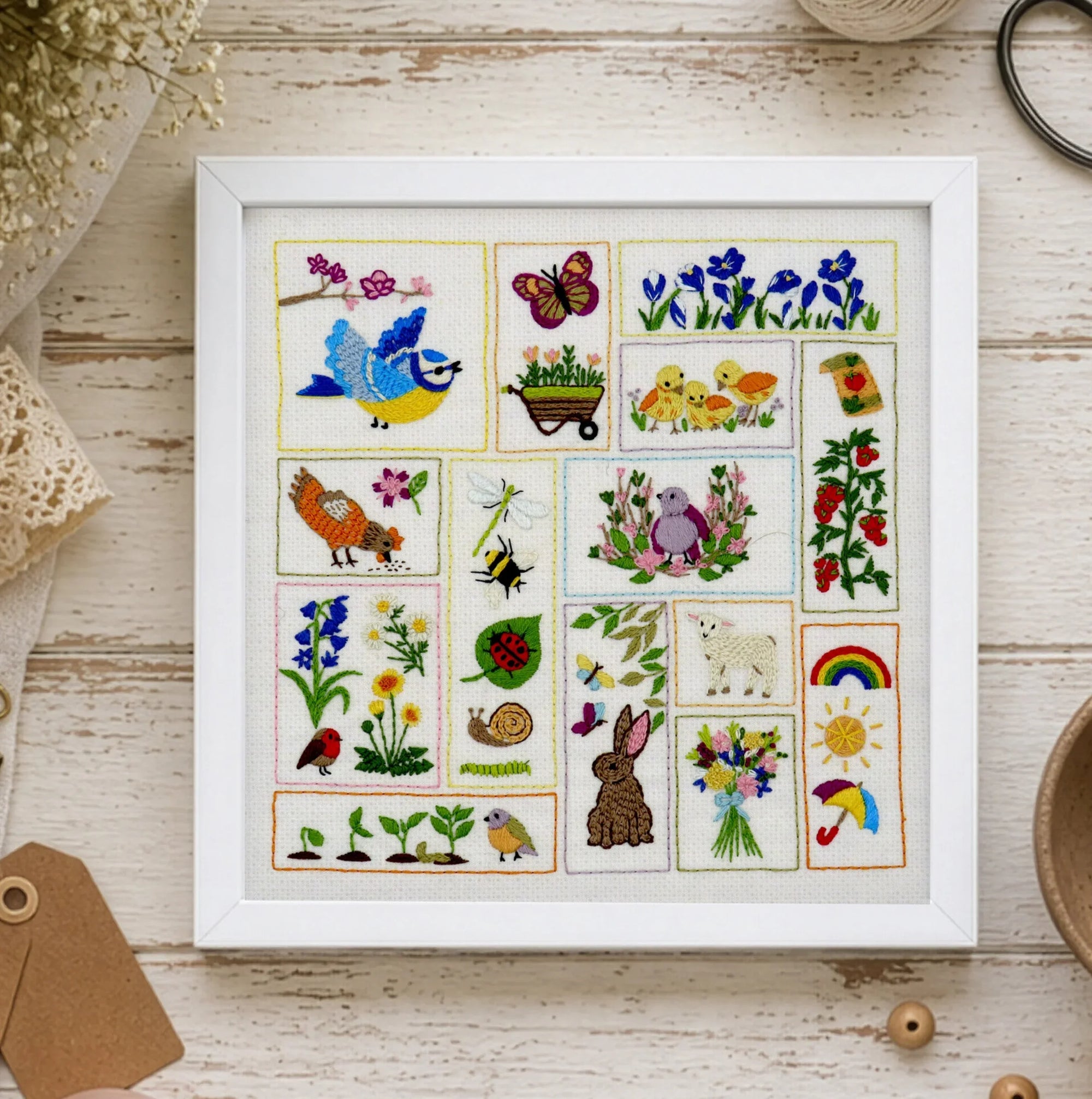 Framed embroidered art with various designs on a wooden surface with crafting supplies.