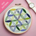 Embroidery hoop with colorful leaf pattern on a pink background, watch on the side.
