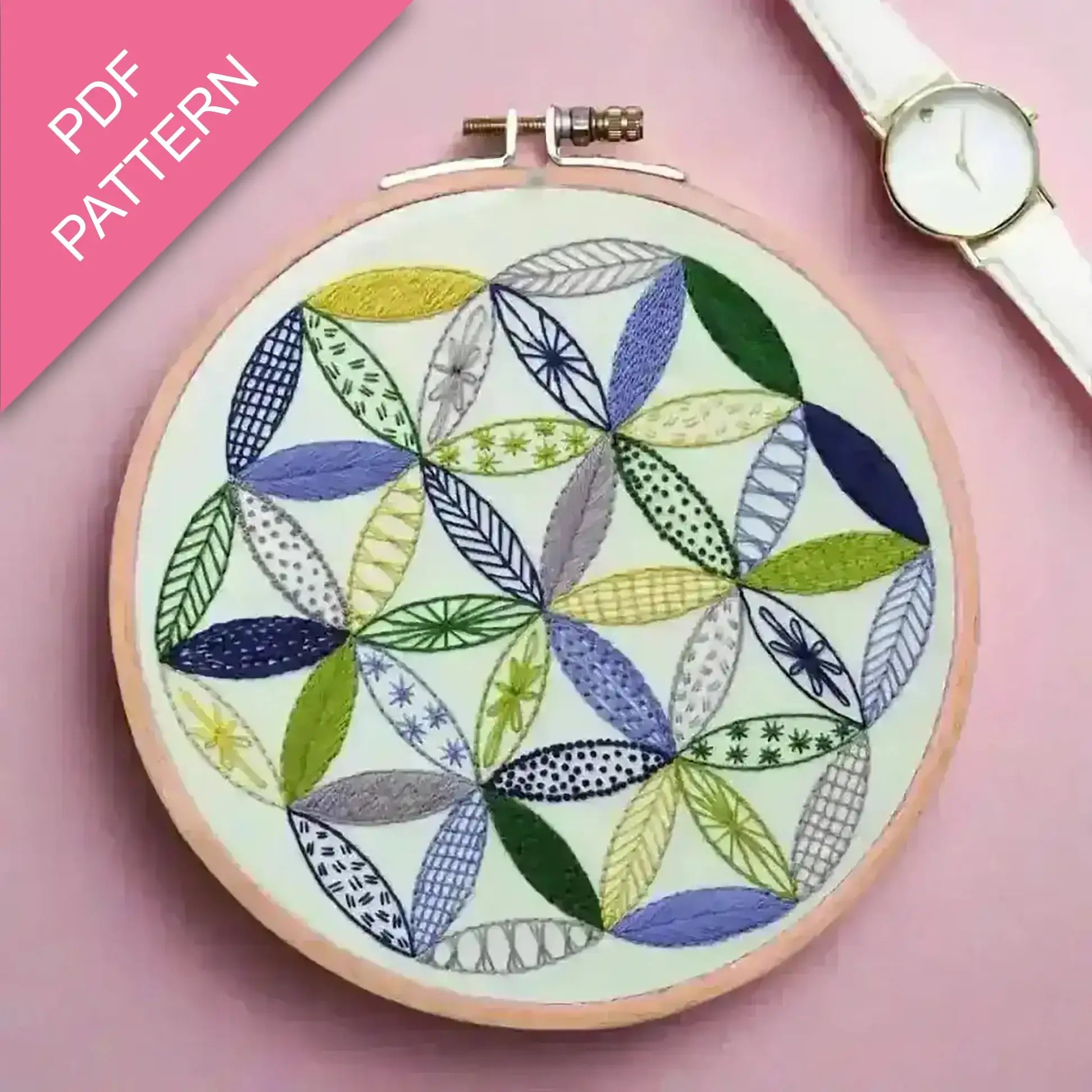 Embroidery hoop with colorful leaf pattern on a pink background, watch on the side.