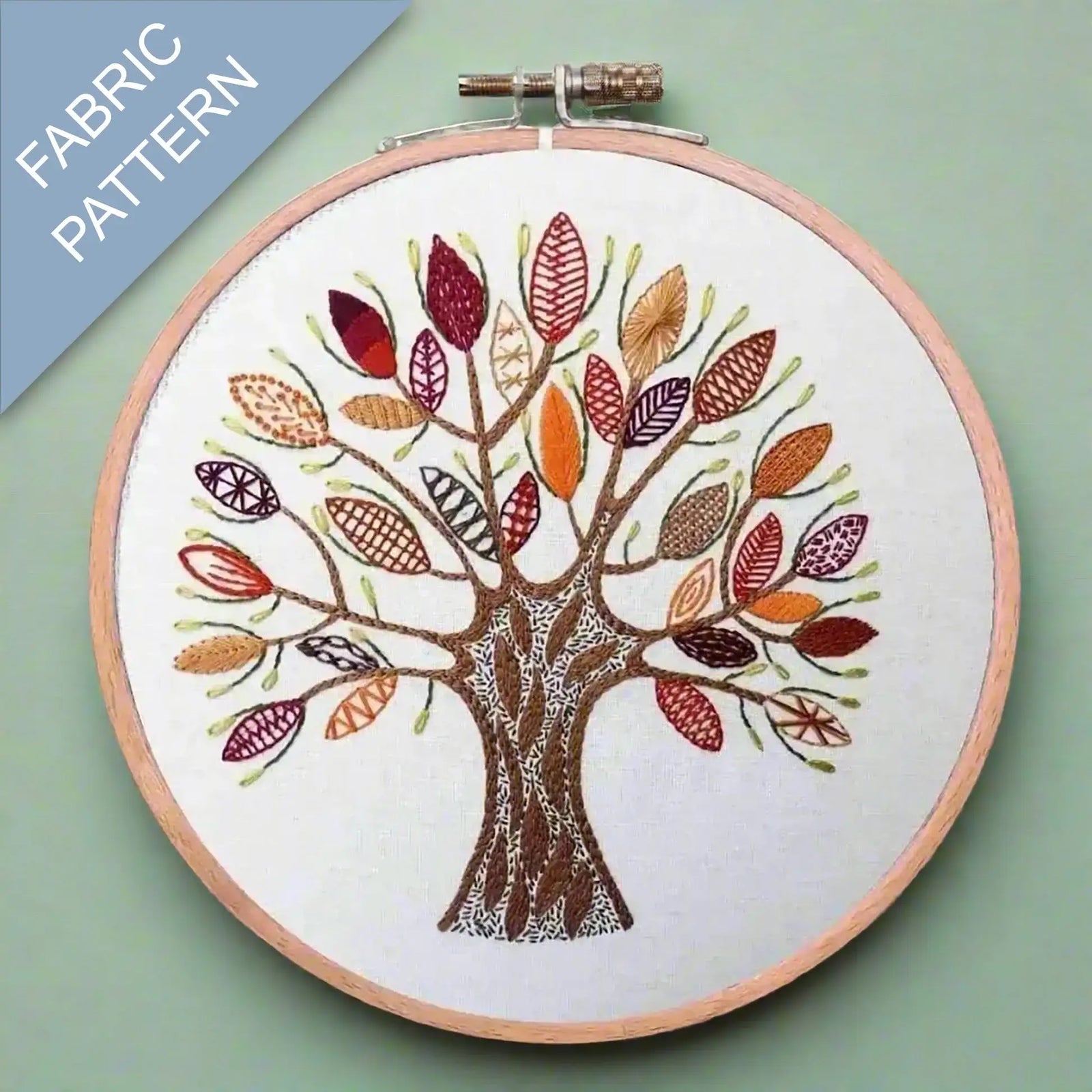 Embroidery hoop with a colorful tree design on fabric against a green background