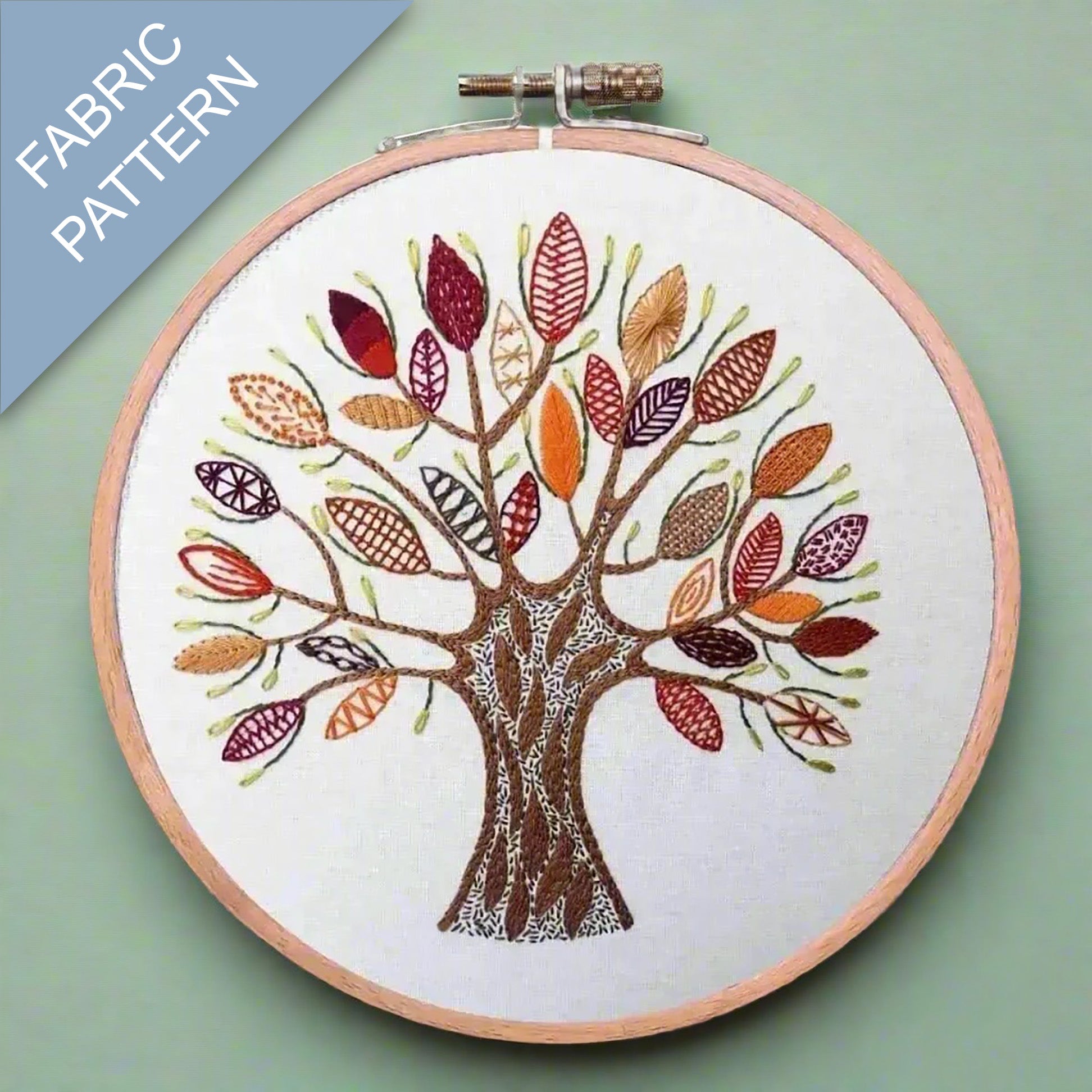 Embroidery hoop with a colorful tree design on fabric against a green background