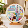 Decorative embroidery hoop with colorful patterns on a table with books, a cup, and plants.