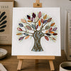 Colorful tree painting on a small easel with a cup of coffee, notebook, and lamp in the background.
