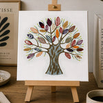 Colorful tree painting on a small easel with a cup of coffee, notebook, and lamp in the background.