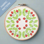 Embroidery hoop with strawberry pattern on fabric, against a gray background.