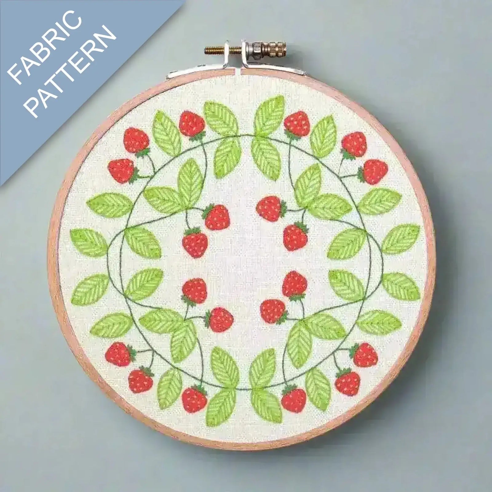 Embroidery hoop with strawberry pattern on fabric, against a gray background.