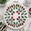 Embroidery hoop with strawberry pattern on a white surface with embroidery supplies.