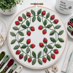 Embroidery hoop with strawberry pattern on a white surface with embroidery supplies.