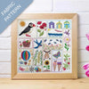 Framed fabric pattern with puffin, flowers, houses, and other elements on a wooden surface.