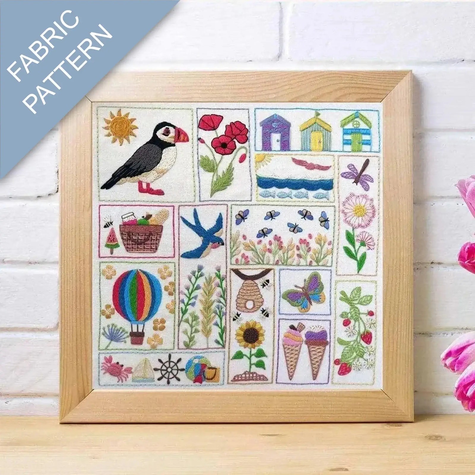 Framed fabric pattern with puffin, flowers, houses, and other elements on a wooden surface.