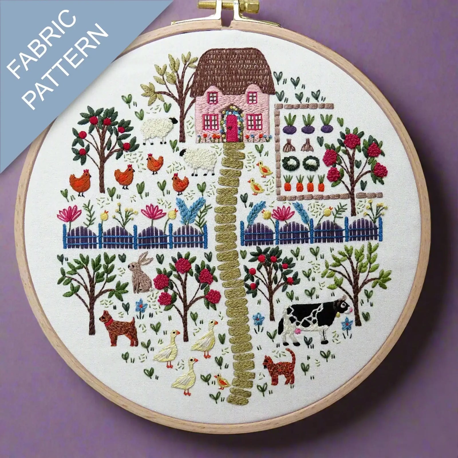 Embroidery hoop with a colorful fabric pattern of a village scene on a purple background.