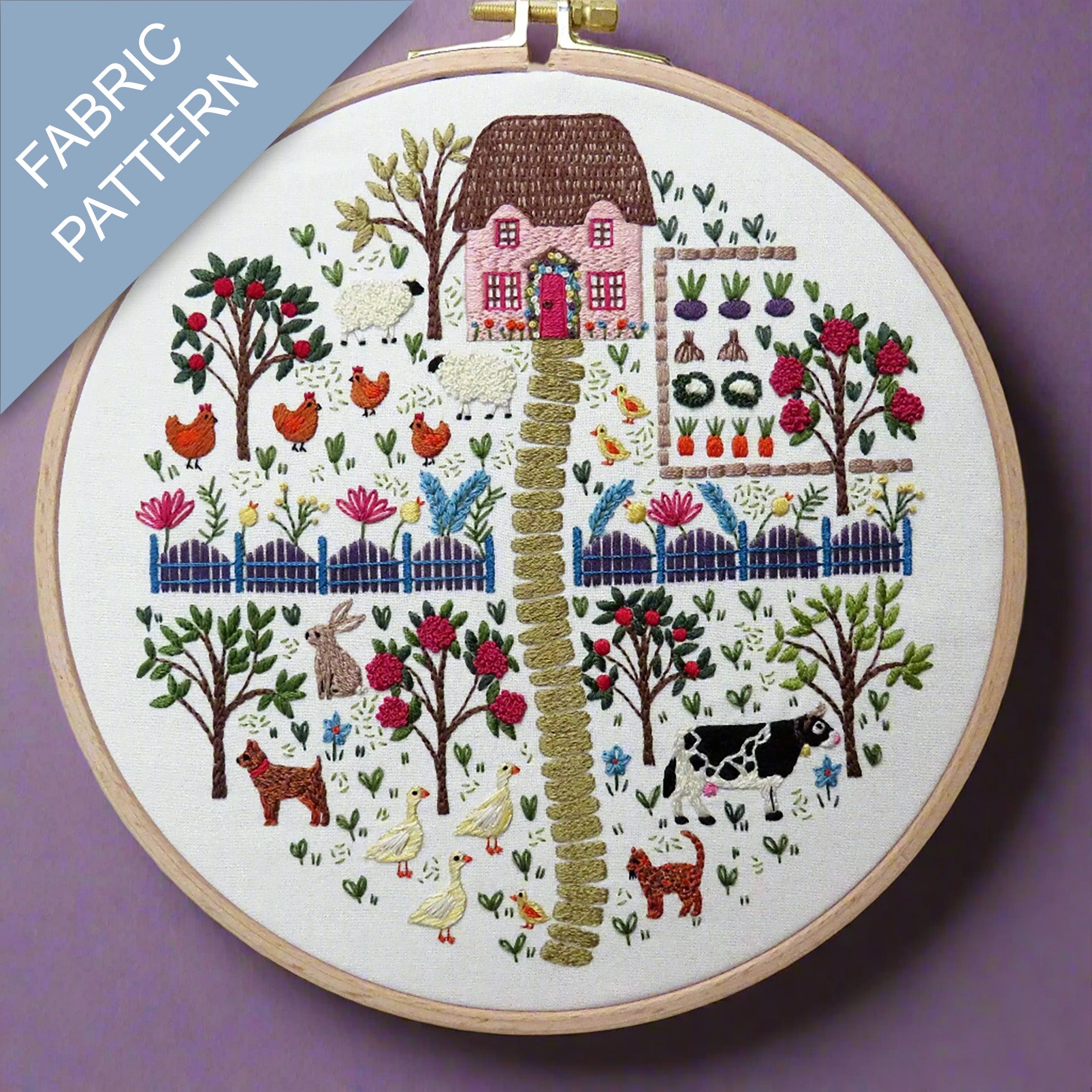 Embroidery hoop with a colorful fabric pattern of a village scene on a purple background.