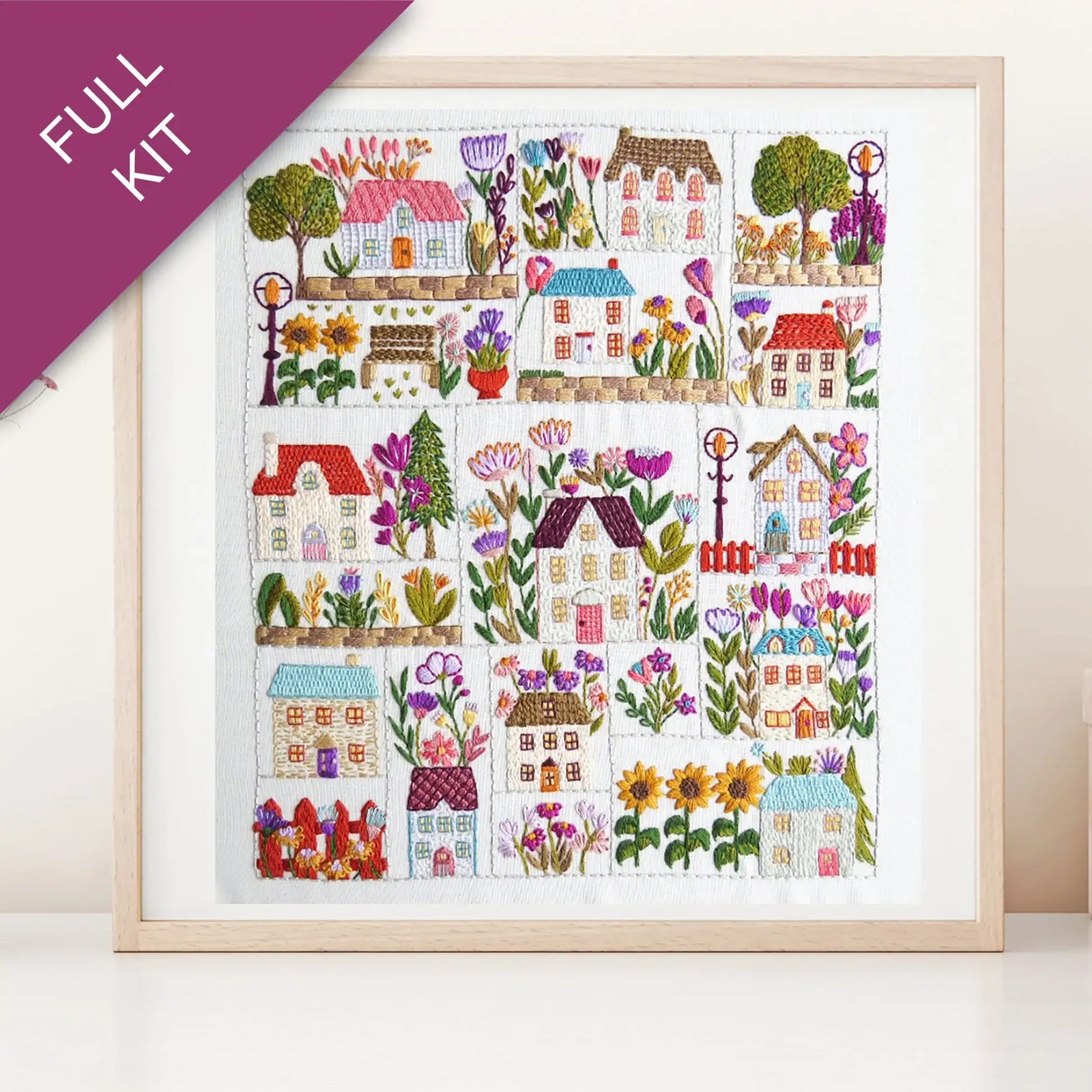 Framed cross-stitch pattern with colorful houses and flowers on a white background