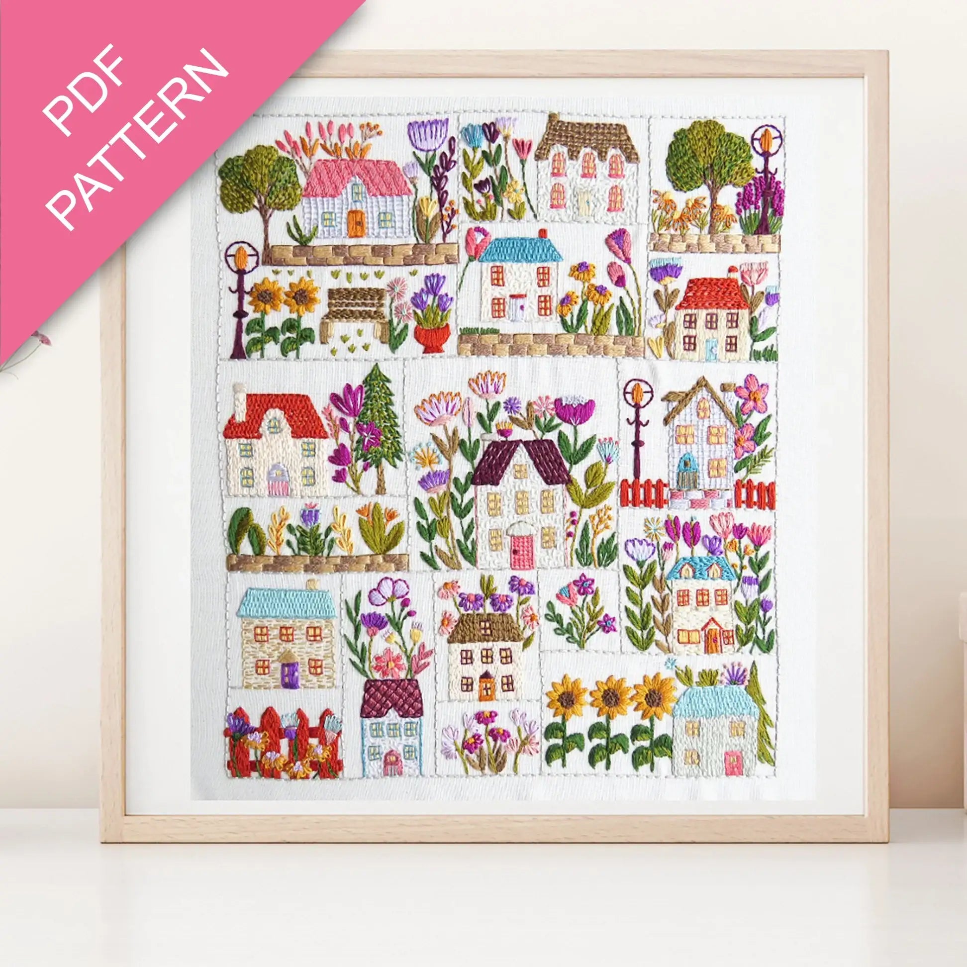 Framed cross-stitch pattern with colorful houses and flowers on a white background
