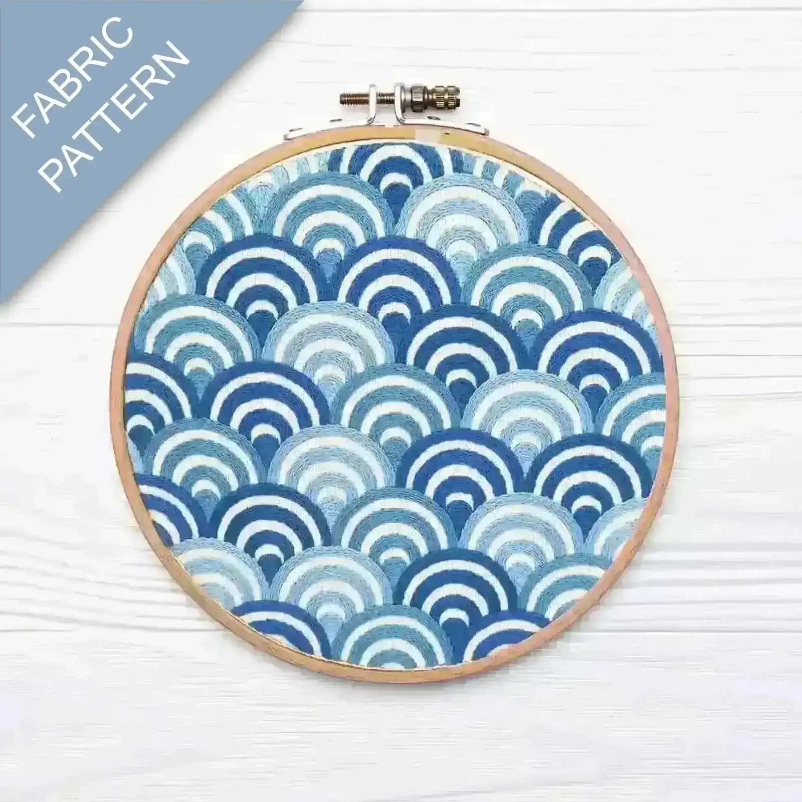 Embroidery hoop with blue and white fabric pattern on a light wooden surface