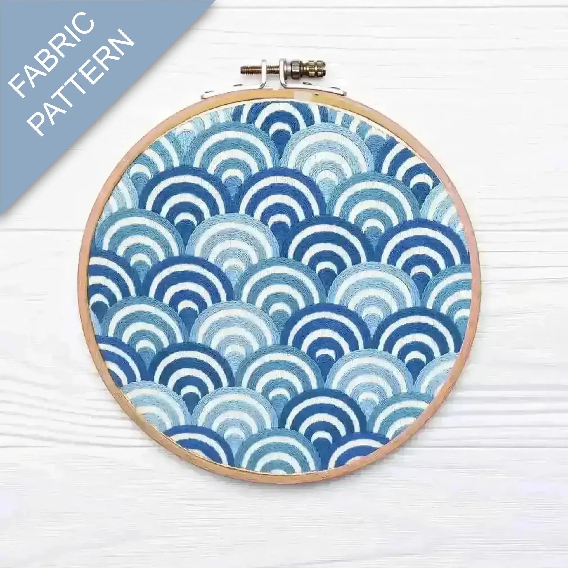 Embroidery hoop with blue and white fabric pattern on a light wooden surface