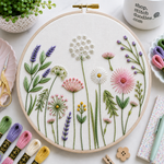Embroidery hoop with floral design surrounded by embroidery supplies on a light surface.