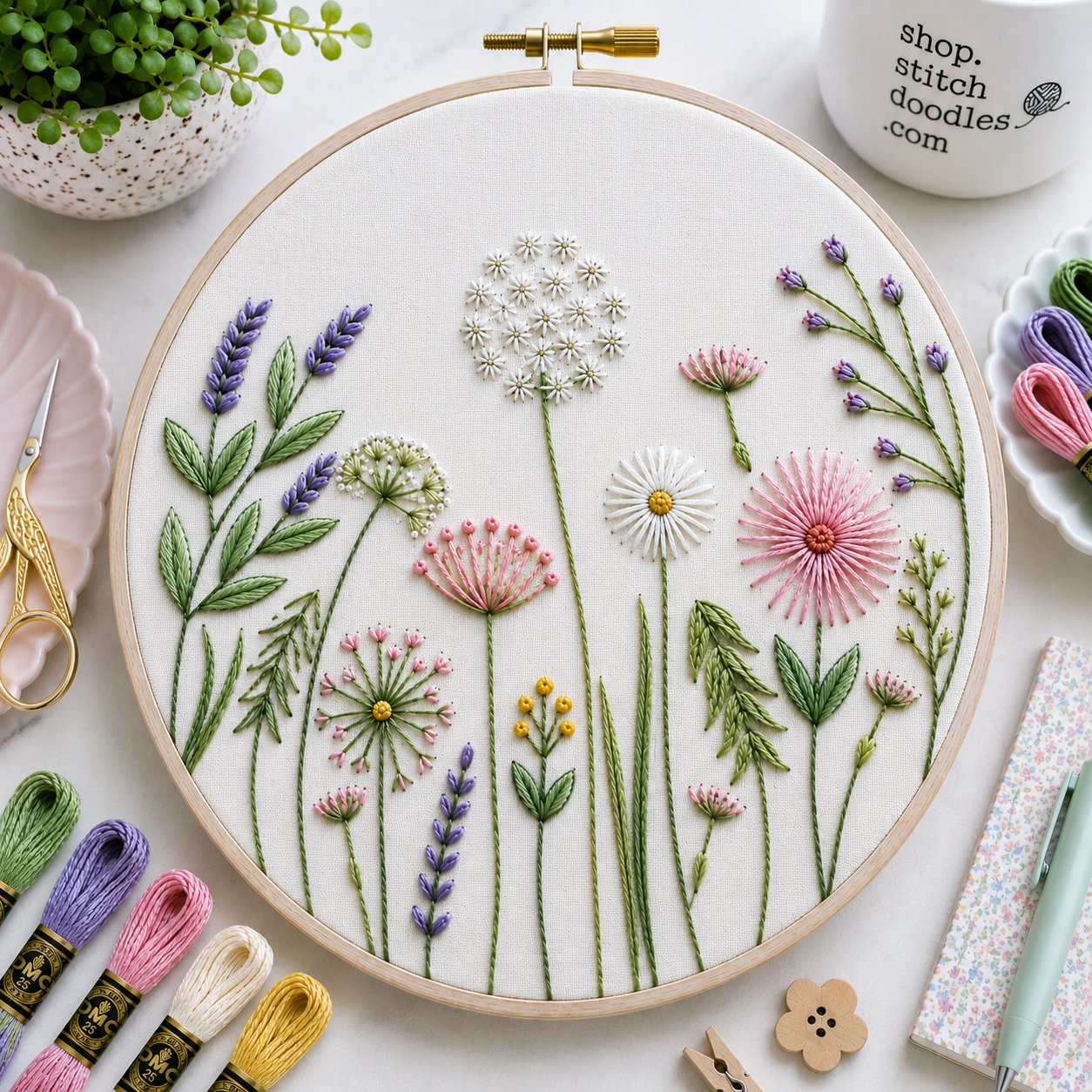 Embroidery hoop with floral design surrounded by embroidery supplies on a light surface.