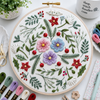 Embroidery hoop with floral and leaf pattern on a white surface with embroidery supplies.
