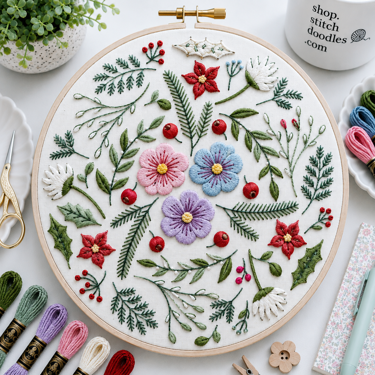 Embroidery hoop with floral and leaf pattern on a white surface with embroidery supplies.