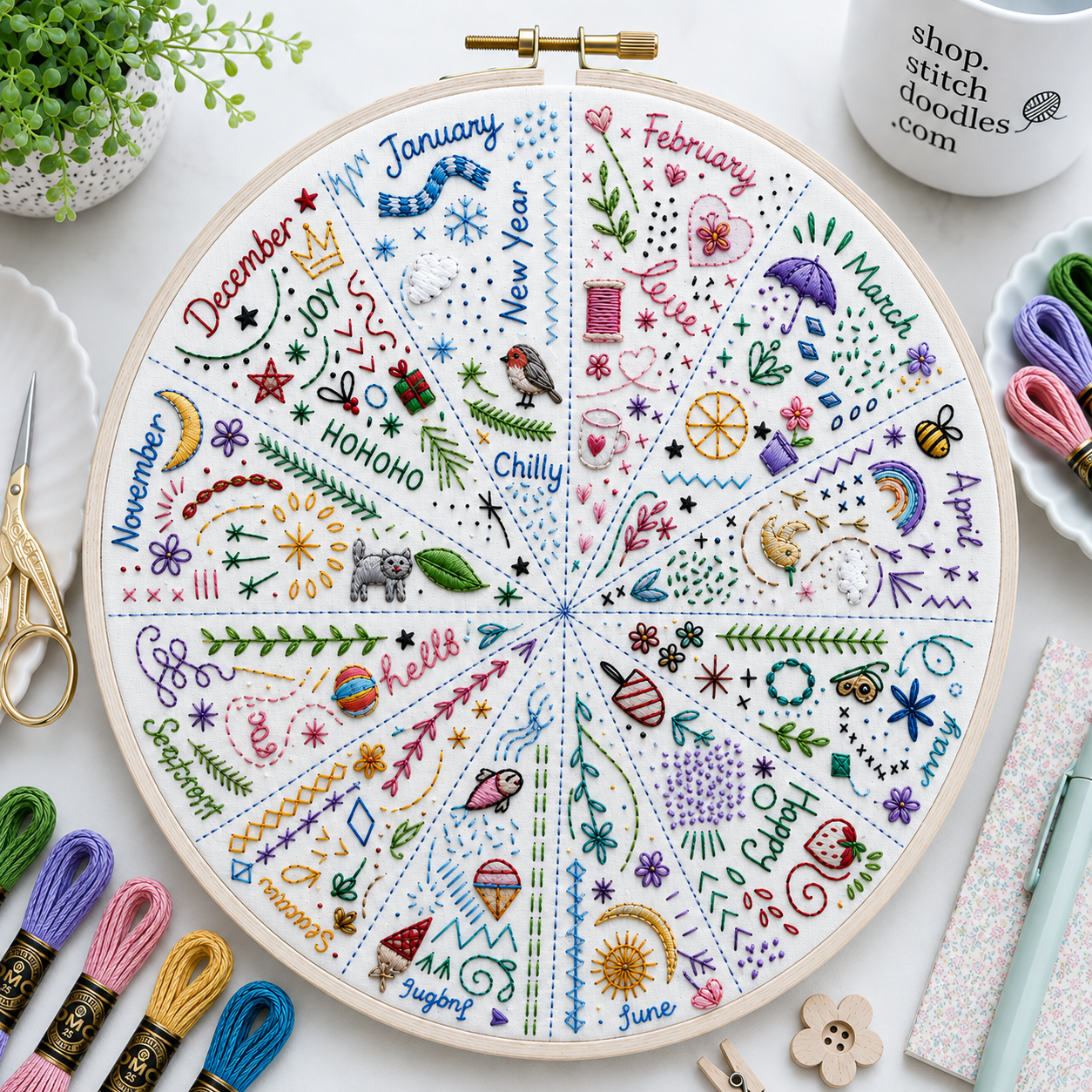Embroidery hoop with a colorful monthly calendar design on a white surface with embroidery supplies.
