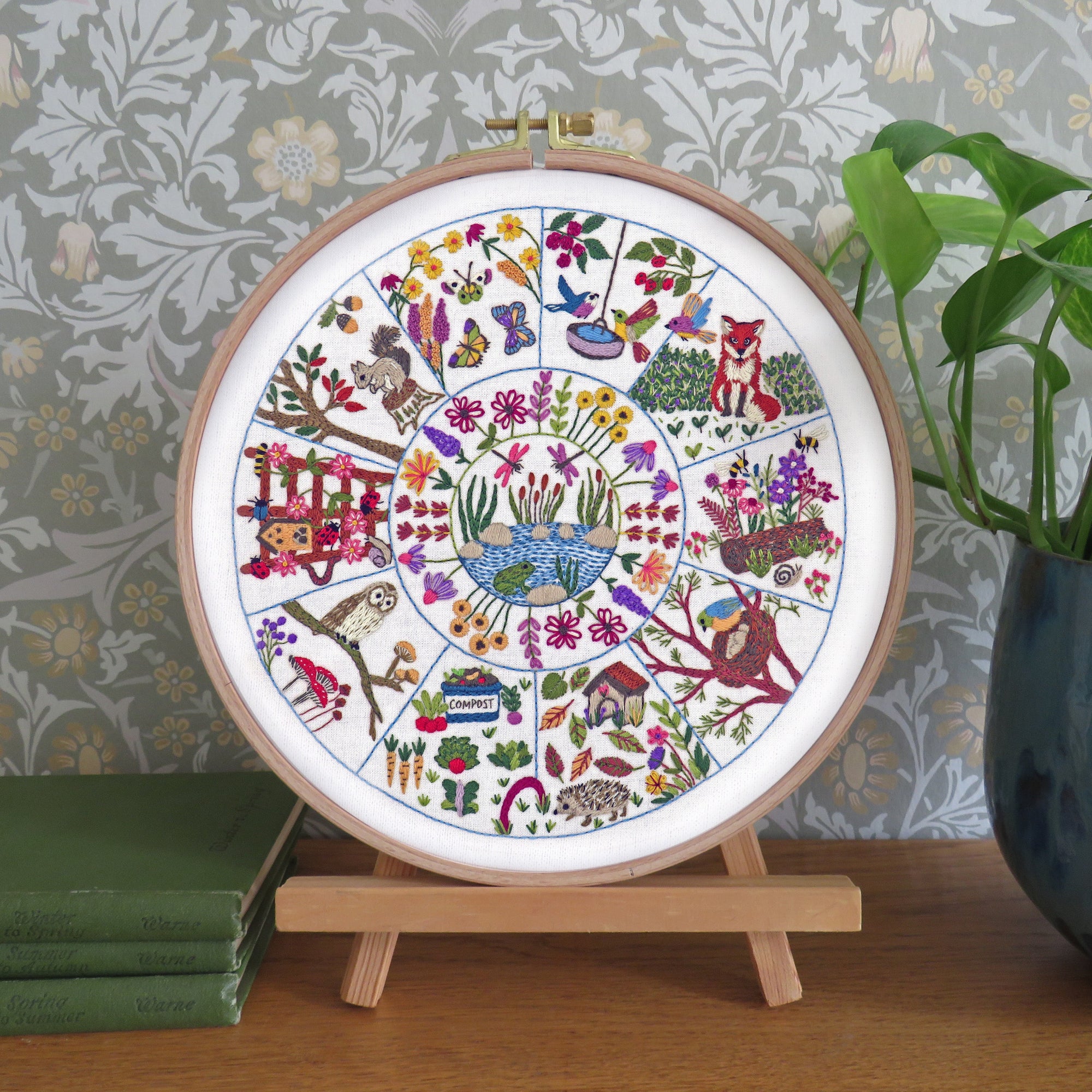Decorative embroidery hoop with colorful patterns on a wooden stand against a patterned wall.