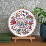 Decorative embroidery hoop with colorful patterns on a wooden stand against a patterned wall.